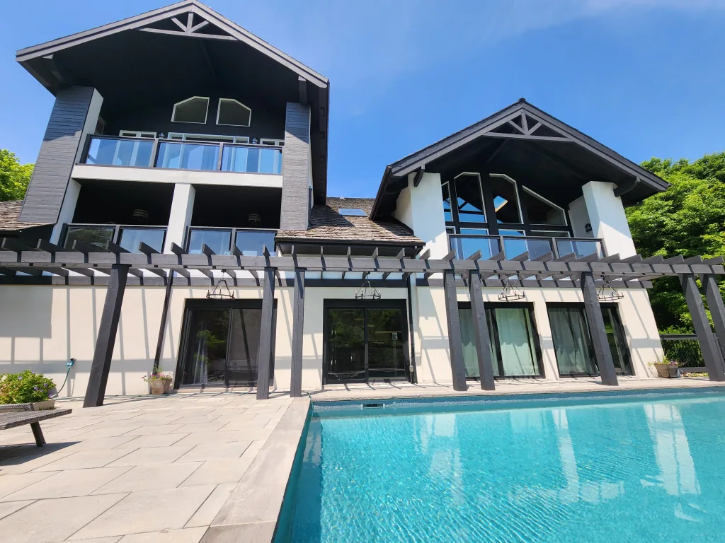 Exterior painting by Sigma Painting — stucco and exposed-beam elevation with glass balconies above a pool